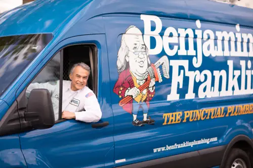 A Benjamin Franklin Plumbing Tech sitting in his work van looking out his window